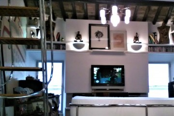 Area tv-musica-lettura. Sistema di illuminazione diversificato tra apparecchiature a sospensione e applique integrato da pannelli e strisce a led